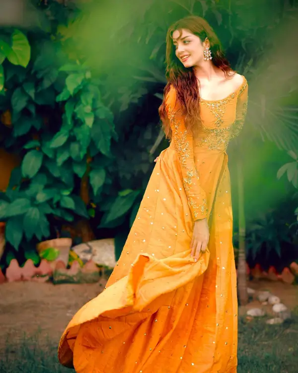The actress wears an orange dress as she sits in a garden