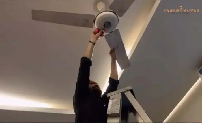 Yasir cleaning a ceiling fan in the living room