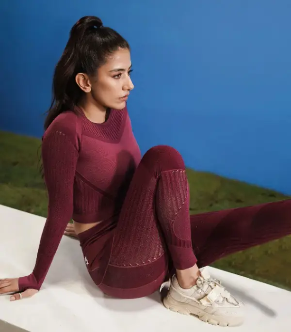 The actress wears a maroon laggy and white sneakers while sitting on a bench