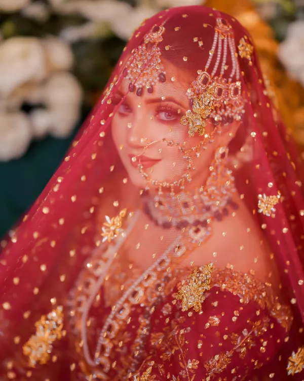 Rabeeca Khan's bridal portrait, veiled in a delicate red dupatta with golden embroidery.