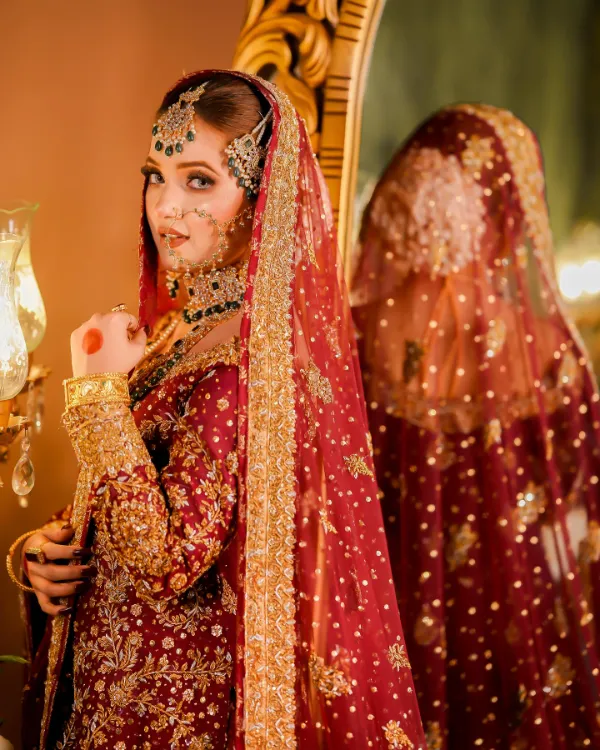 Rabeeca Khan in a traditional bridal pose, veiled, with a focus on her elaborate jewelry.