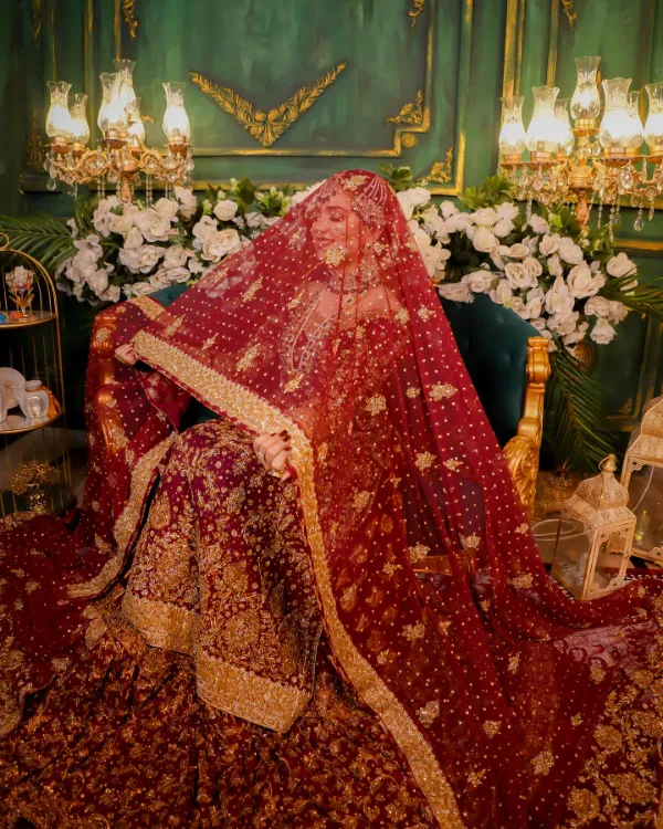 Rabeeca Khan under a sheer red bridal veil, with a serene expression and detailed adornments